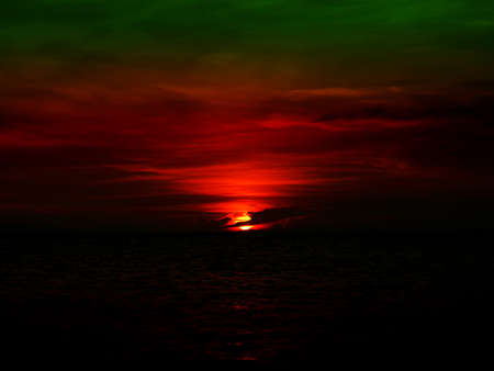 sunset last light of sun on horizontal line over dark green sky and oceanの写真素材