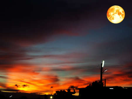 full blood moon on colorful sky in orange and dark gray cloud silhouette buildingの写真素材
