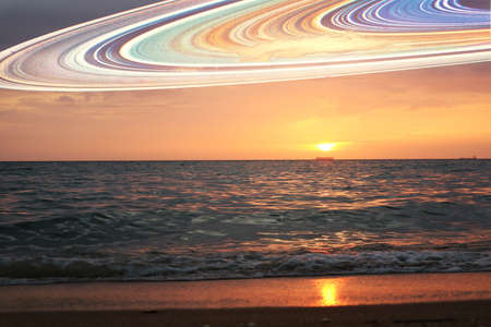 sunset and saturn ring on horizontal sea water surface colorful cloud sky.の写真素材