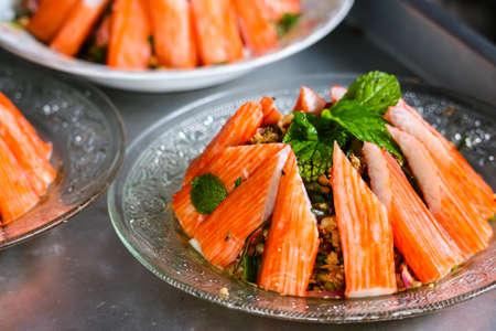 spicy minced crab sticks salad and mint leaves on top and glass dishの写真素材