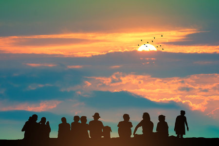 Silhouette people sitting on the top mountain and sunset on the colorful sky orange cloud and birds flying, concept family party on holiday, party outdoor in weekendの写真素材