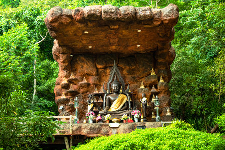 A tranquil Buddha statue rests beneath a natural stone canopy, surrounded by lush greenery. This serene scene evokes feelings of peace and spirituality.の写真素材