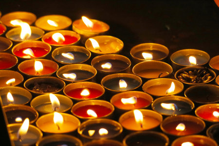 A vibrant arrangement of colorful candles with flickering flames on a dark surface. This image captures warmth and tranquility, ideal for spiritual or decorative themes.の写真素材