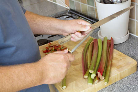 Male cook sharpening knife on a steel in a domestic kitchen  There is rhubarb on the chopping board の写真素材