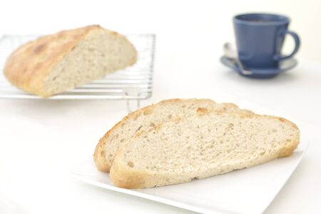 slices of homemade garlic and rosemary focaccia bread on a plate, with the cut loaf on a cooling...