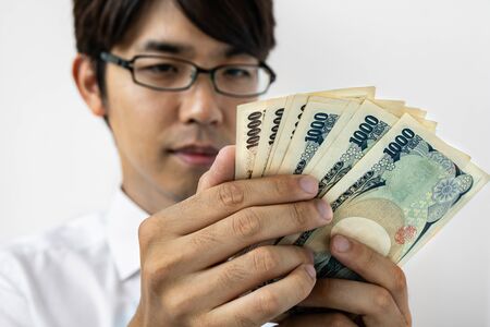 Young Japanese businessman counting money. Holding a stack of japanese yen banknotes. Isolated on white.の写真素材