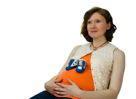 Pregnant adult woman playing with baby shoes sitting on a chairの写真素材