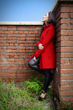 Beautiful woman in a red coat on a brick wall in the cityの写真素材