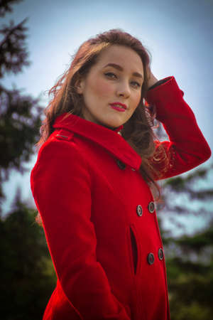 Beautiful girl in a red coat on a background of treesの写真素材