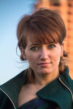 Portrait of a young beautiful girl in a dark green coat outdoor at sunset