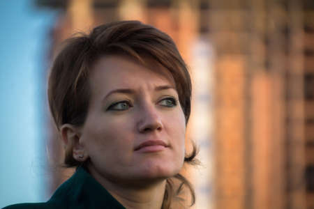 Portrait of a young beautiful girl in a dark green coat outdoor at sunsetの写真素材