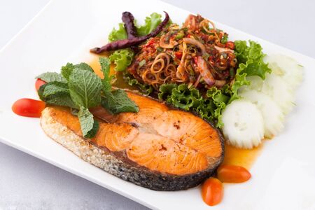 fried salmon fish with spicy salad on whith plateの写真素材