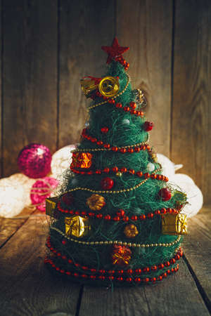 Handmade decorative Christmas Tree on rustic wooden board. Soft bokeh lights in the background. This can be used as Christmas or New Year's greeting card.の写真素材