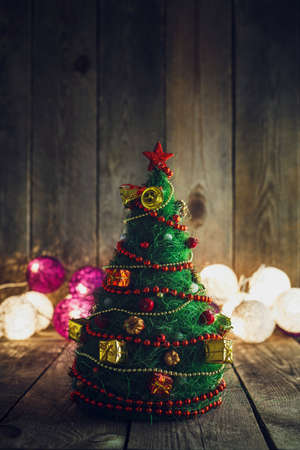 Handmade decorative Christmas Tree on rustic wooden board. Soft bokeh lights in the background. This can be used as Christmas or New Year's greeting card.の写真素材