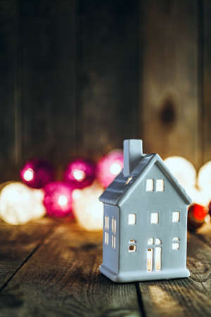 Christmas background white house shaped ceramics candle holder on wooden board. Soft lights in the background. This can be used as Christmas or New Year's greeting card.の写真素材