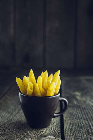 Close-up of bright yellow pasta penne on a wooden backgroundの写真素材