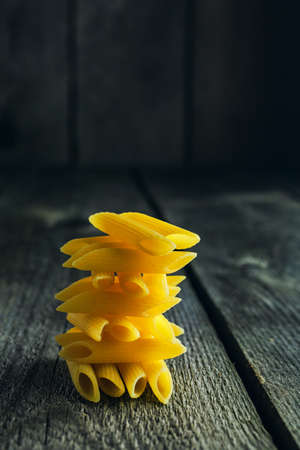 Close-up of bright yellow pasta penne stacked in a tower shape on a wooden backgroundの写真素材