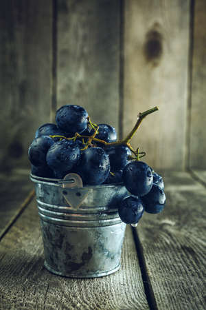 Close-up of blue grapes in small bucket on a wooden backgroundの写真素材