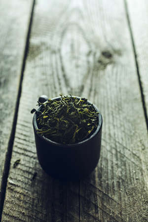 Dry organic green tea leafs in a black cup on a wooden backgroundの写真素材