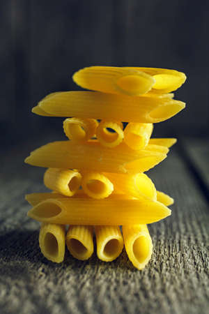Close-up of bright yellow pasta penne stacked in a tower shape on a wooden backgroundの写真素材