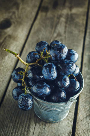Close-up of blue grapes in small bucket on a wooden backgroundの写真素材