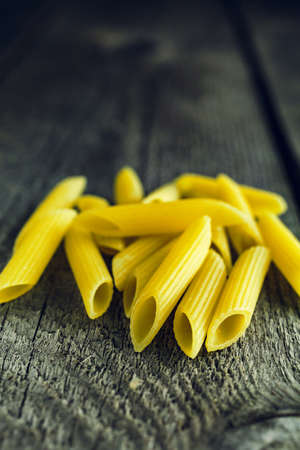 Close-up of bright yellow pasta penne on a wooden backgroundの写真素材