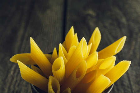 Close-up of bright yellow pasta penne on a wooden backgroundの写真素材