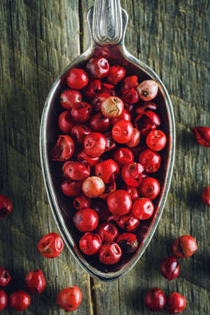 Pink pepper in a spoon on a wooden background. Macro shot.