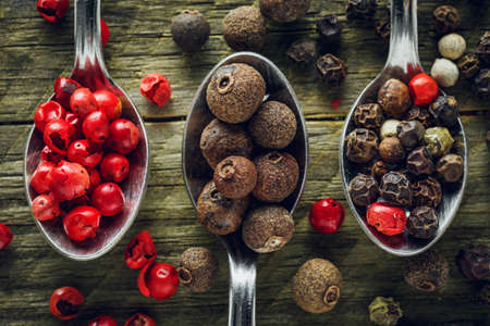 Pepper mix in a spoons on a wooden background. Macro shot.