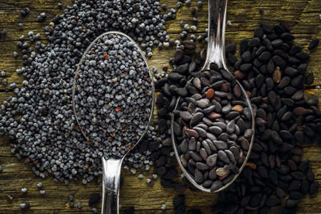 Poppy and black sesame seeds in a spoons on a wooden background. Macro shot. Top view.