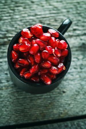 Ripe pomegranate seeds in a small cup on a vintage wooden backgroundの写真素材
