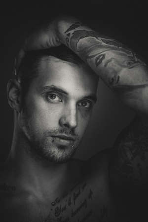 Young handsome man with tattoos and piercings. Fine film grain texture. Studio shot.の写真素材