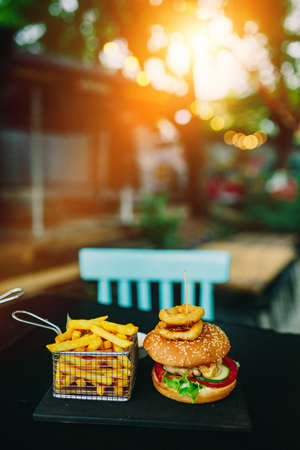 Burger and French Fries and onion rings on cafe table. Soft focus, fine film gain texture.