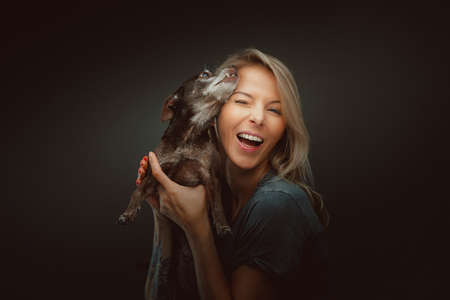 Young pretty woman with her Toy Terrier dog. Studio shot. Moody dark lighting, dark background.の写真素材