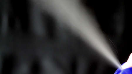 Aerosol can being sprayed against a black background.の写真素材