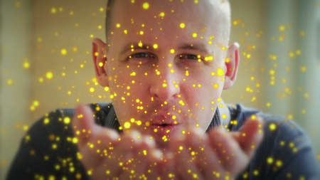a young man blows off his hands with beautiful colored particlesの写真素材