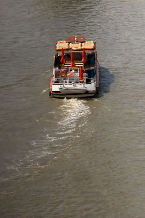 Rear high angle view of the wake and deck of a boat travelling on a dirty river in muddy brown waterの写真素材