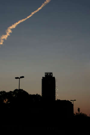 Jet trail in the sky over a city at sunset with the modern skyscrapers silhouetted against the setting sun at dusk, with copyspaceの写真素材