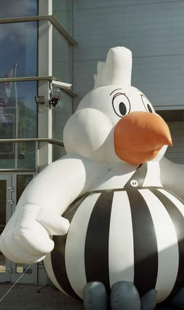 Inflated chicken mascot with a striped black and white round belly and orange beak standing outside a commercial buildingの写真素材