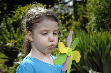 Cute girl blows at colorful spinner in the garden.の写真素材