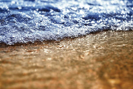 Small waves with bubbles on the sunny beach