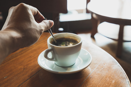 Men make black coffee in a white coffee mug placed on a brown wood table.の写真素材