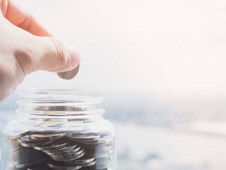 Close up view on the side of the hand holding a coin to put money in a glass bottle For investment...