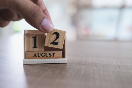 Mother's Day in Thailand, August 12, close up of left hand is picking up a wooden calendar block that is placed on a wooden table and copy spaceの写真素材