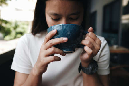 Close up of an Asian woman drinking coffee in a coffee shop