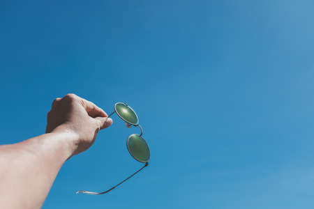 Close up hand of a man holding sunglasses and Blue sky background