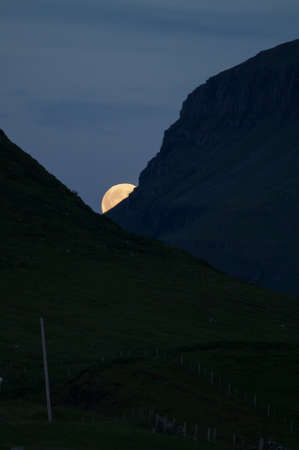 The moon peaks between two mountains during sunset on the isle of Skye, Scotlandの写真素材