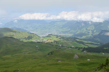 Panoramic view of beautiful landscape in the  Swiss Alps with fresh green meadows and village cottages in the distance.の写真素材