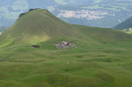 Chalet on mountain slope, rustic cabin in the Alps, with a small lake in front.の写真素材