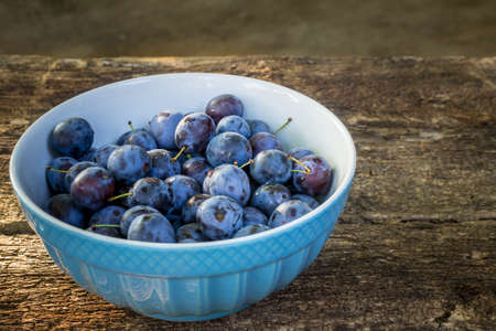 plums in bowl on wooden backgroundの写真素材